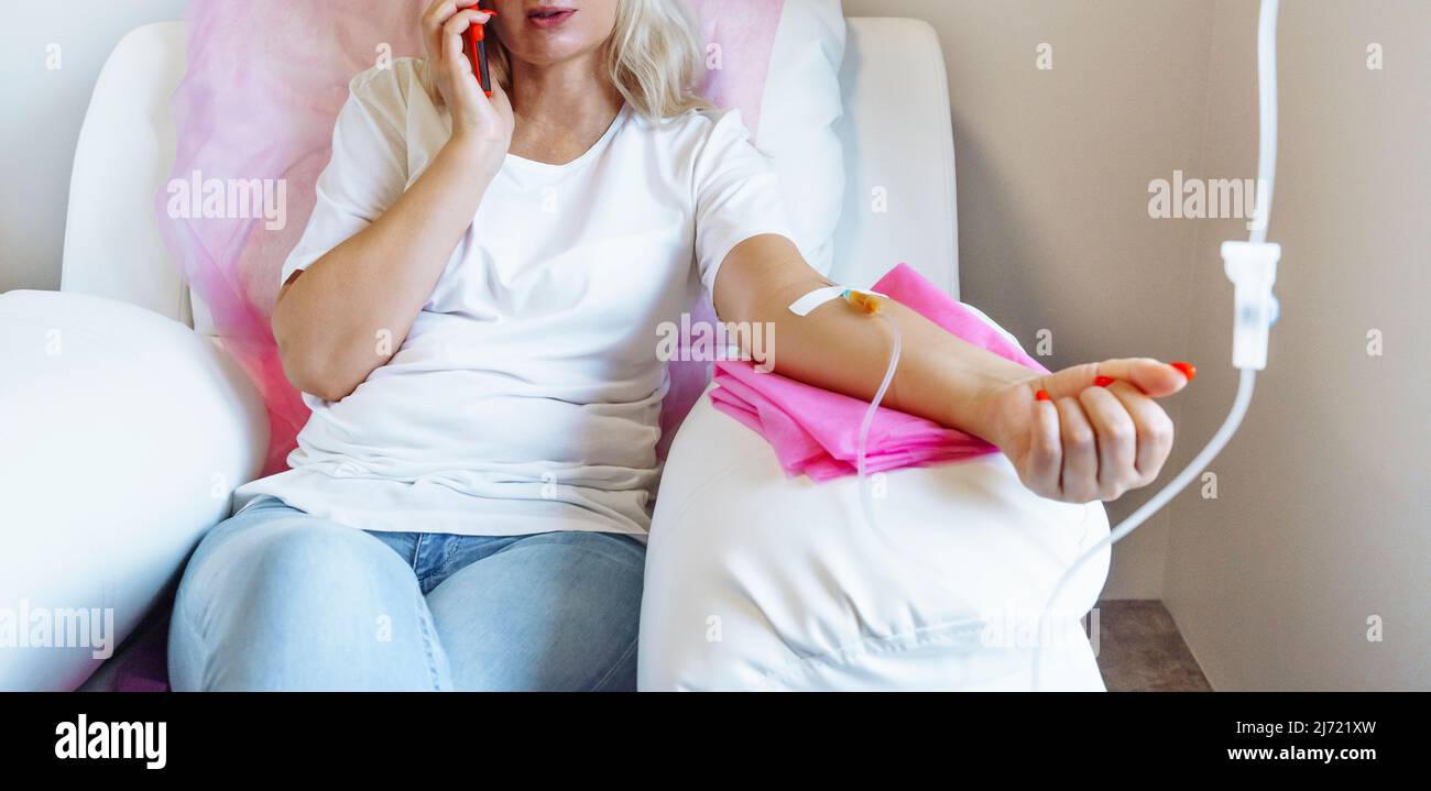 Frau im Krankenhaus spricht am Mobiltelefon, während die Nadel im Arm ist, Vitamin Therapy IV Drip Infusion im Frauenblut Stockfoto