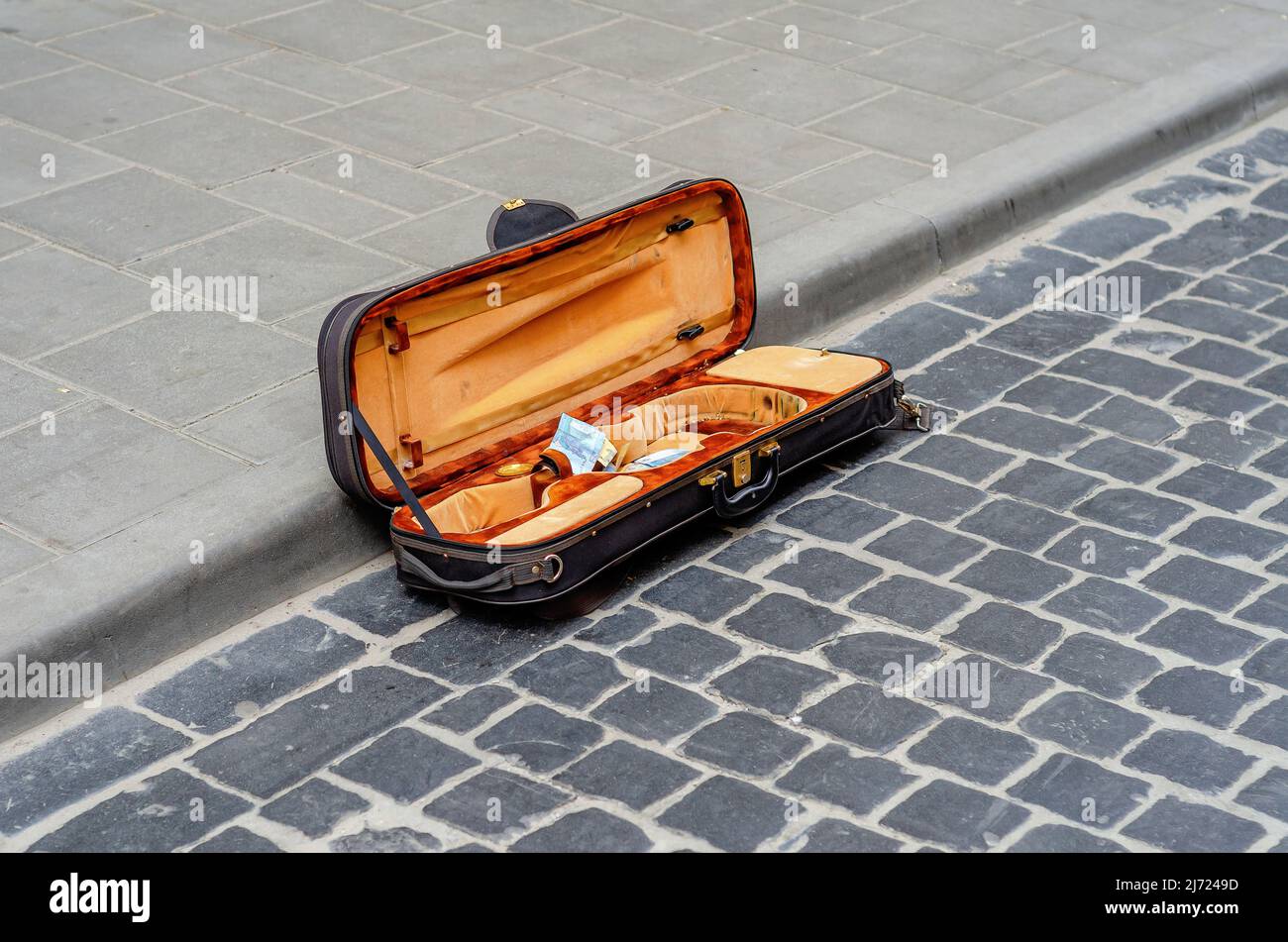 Das offene Geigengehäuse liegt auf altem Kopfsteinpflaster in der Stadt. Straßenmusiker sammelt Geld Stockfoto