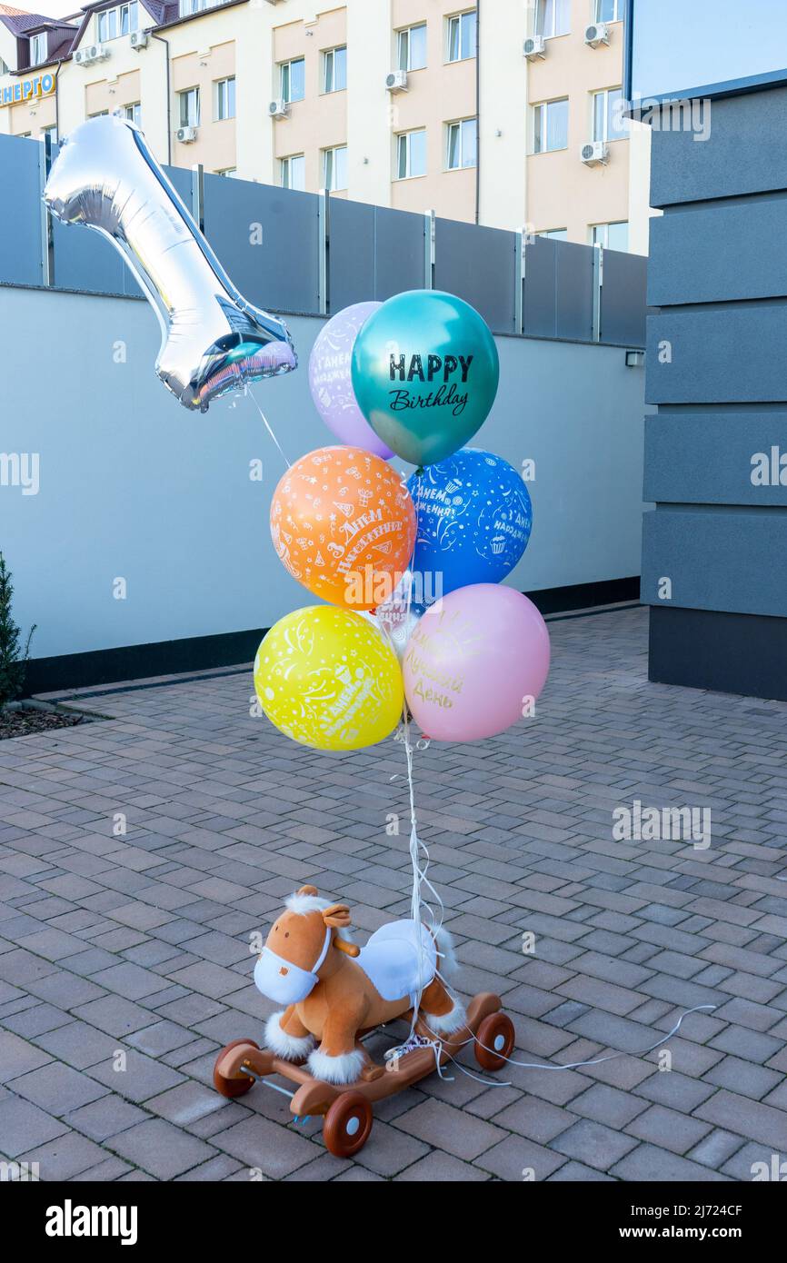 Ein Geschenk für ein Kind im Alter von 1 Jahren. Bunte Luftballons werden an das Pferd eines Kindes gebunden. Stockfoto