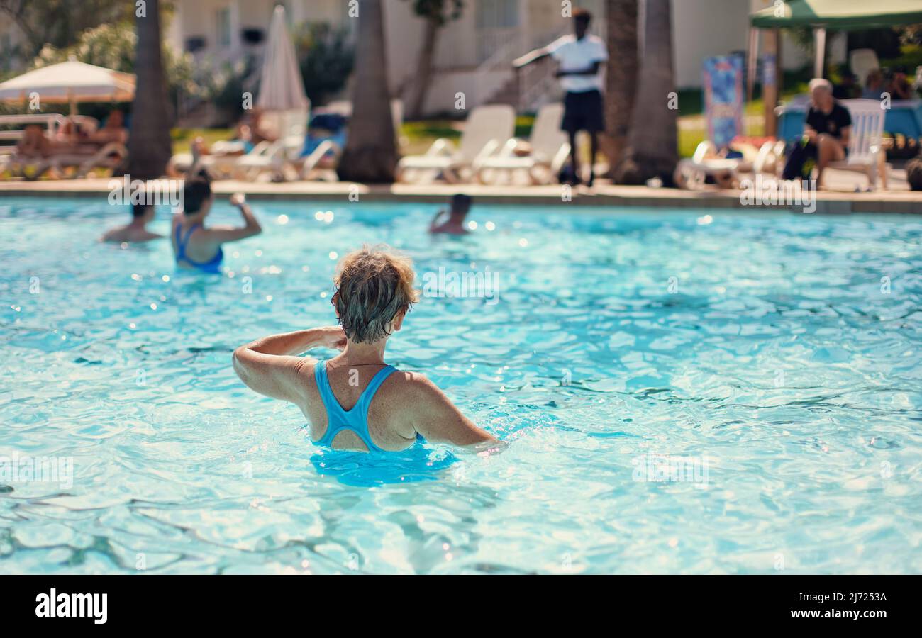 Ältere Frau mit grauen Haaren, in blauem Badeanzug, Wassergymnastik im Hotelpool, Blick von hinten Stockfoto