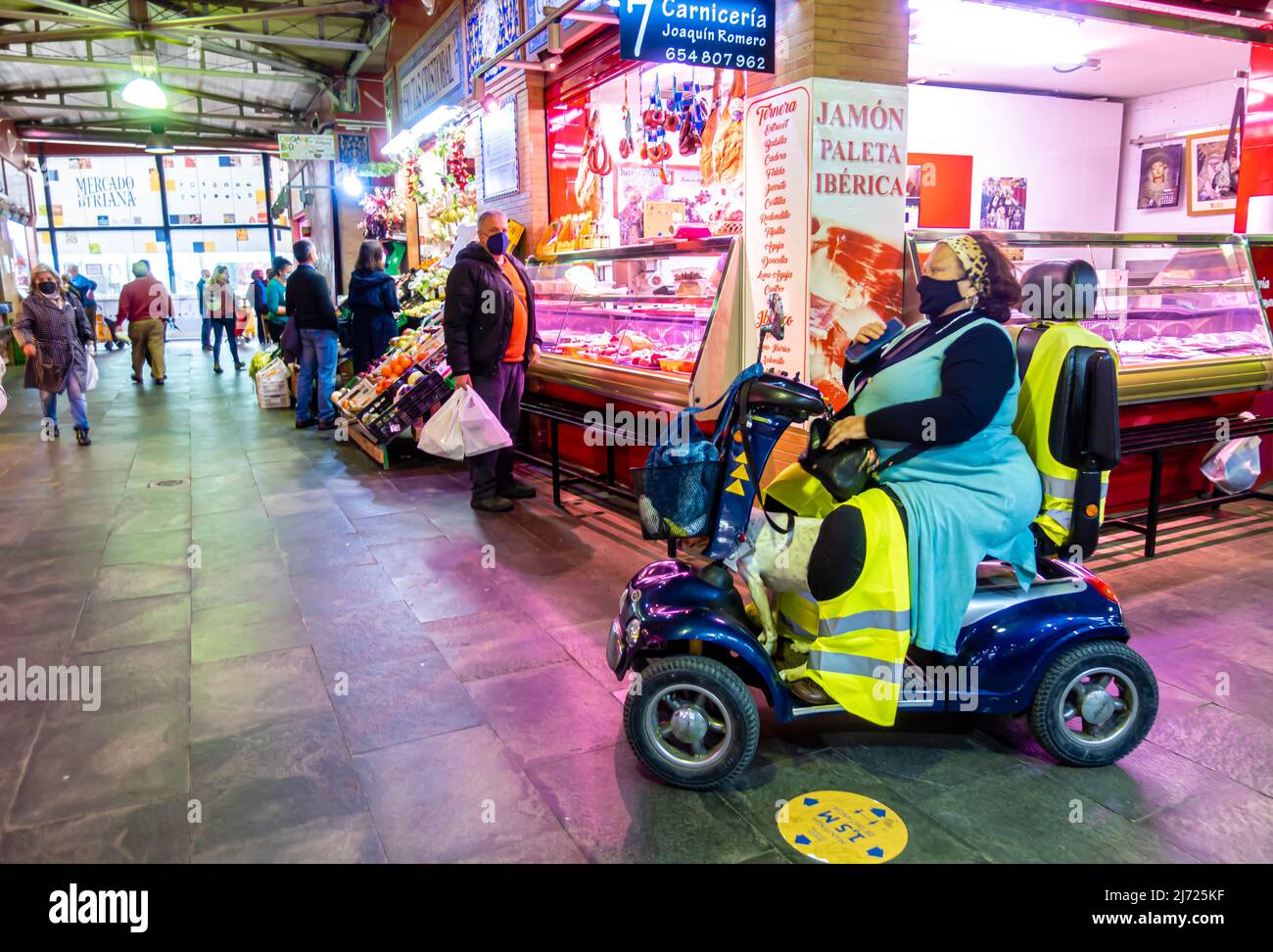 Frau in Gesichtsmaske Reiten Handicap Mobility Scooter in Mercado de Triana, Sevilla, Andalusien, Spanien Stockfoto