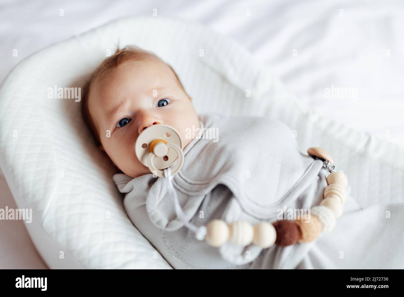 Nettes kaukasisches blondes Baby zwei Monate alt, das zu Hause im Kokon liegt und Nippel saugt. Stockfoto