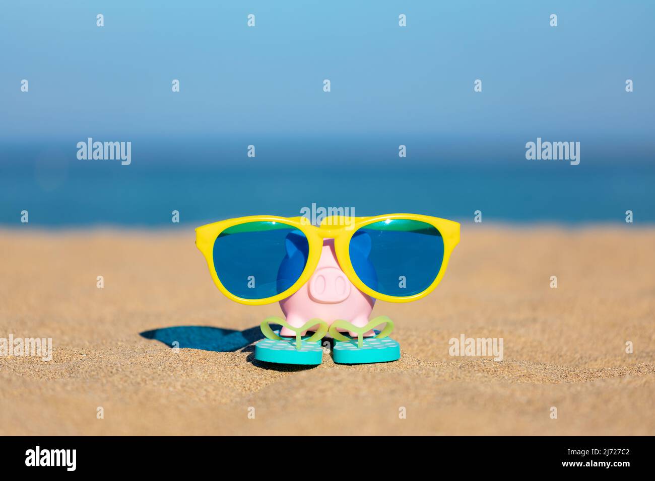 Sparschwein am Strand gegen Meer und Himmel Hintergrund. Einsparungen für Sommerreisen und Urlaubskonzept Stockfoto