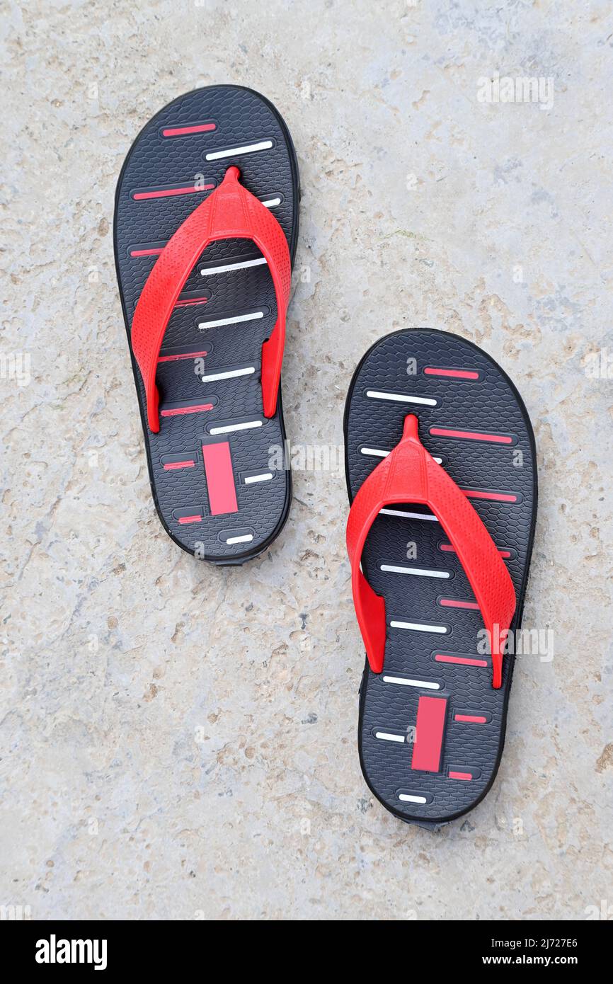 Nahaufnahme des roten schwarzen Slippers auf unscharfem graubraunen Hintergrund. Stockfoto