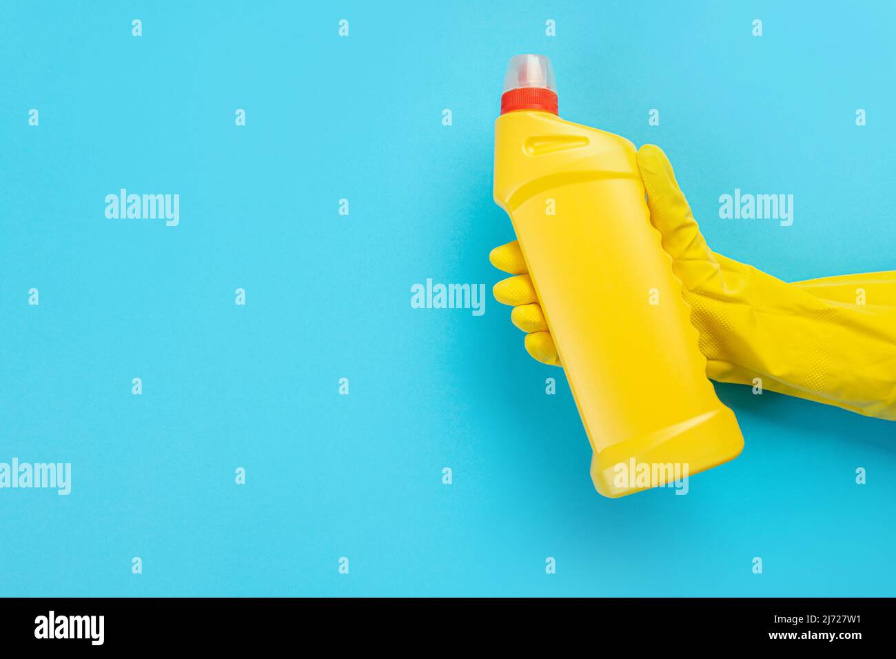 Eine Hand in einem Gummihandschuh hält eine gelbe Flasche Waschmittel auf einem blauen Hintergrund. Banner mit Kopierbereich. Chemische Reiniger, Haushaltschemikalien, brus Stockfoto