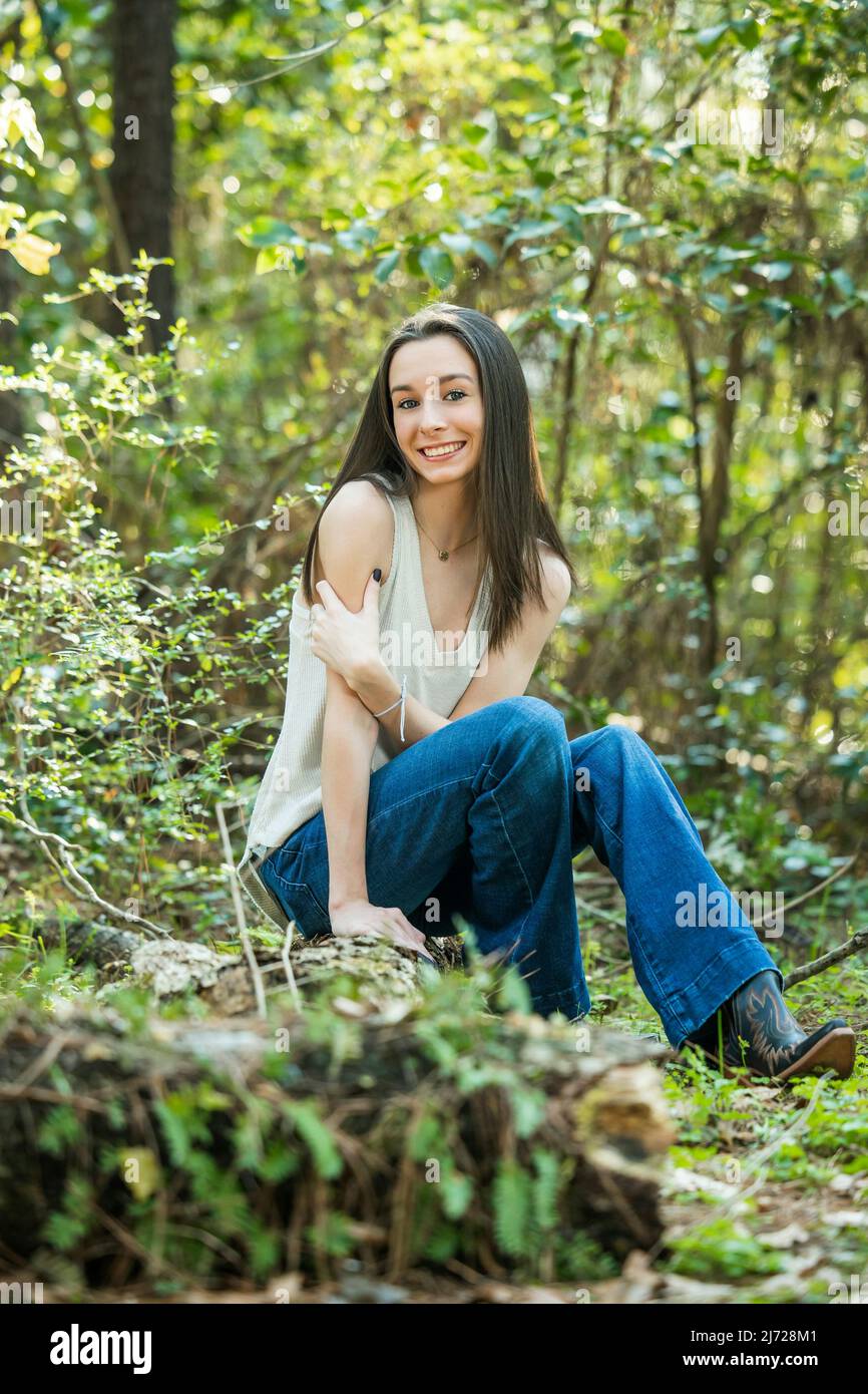 Ein schönes glückliches Teenager Brünette Mädchen im Freien auf einem Holzhackling sitzen und lächeln mit Kopierraum Stockfoto