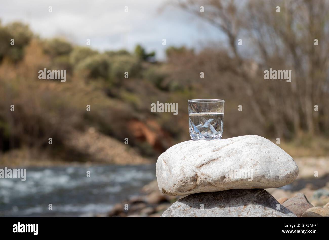 Transparentes und reines Wasser in Glas auf Stein, das die Reinheit der Natur repräsentiert. Warum es vor dem Hintergrund der Natur und des Flusses gepflegt werden muss Stockfoto