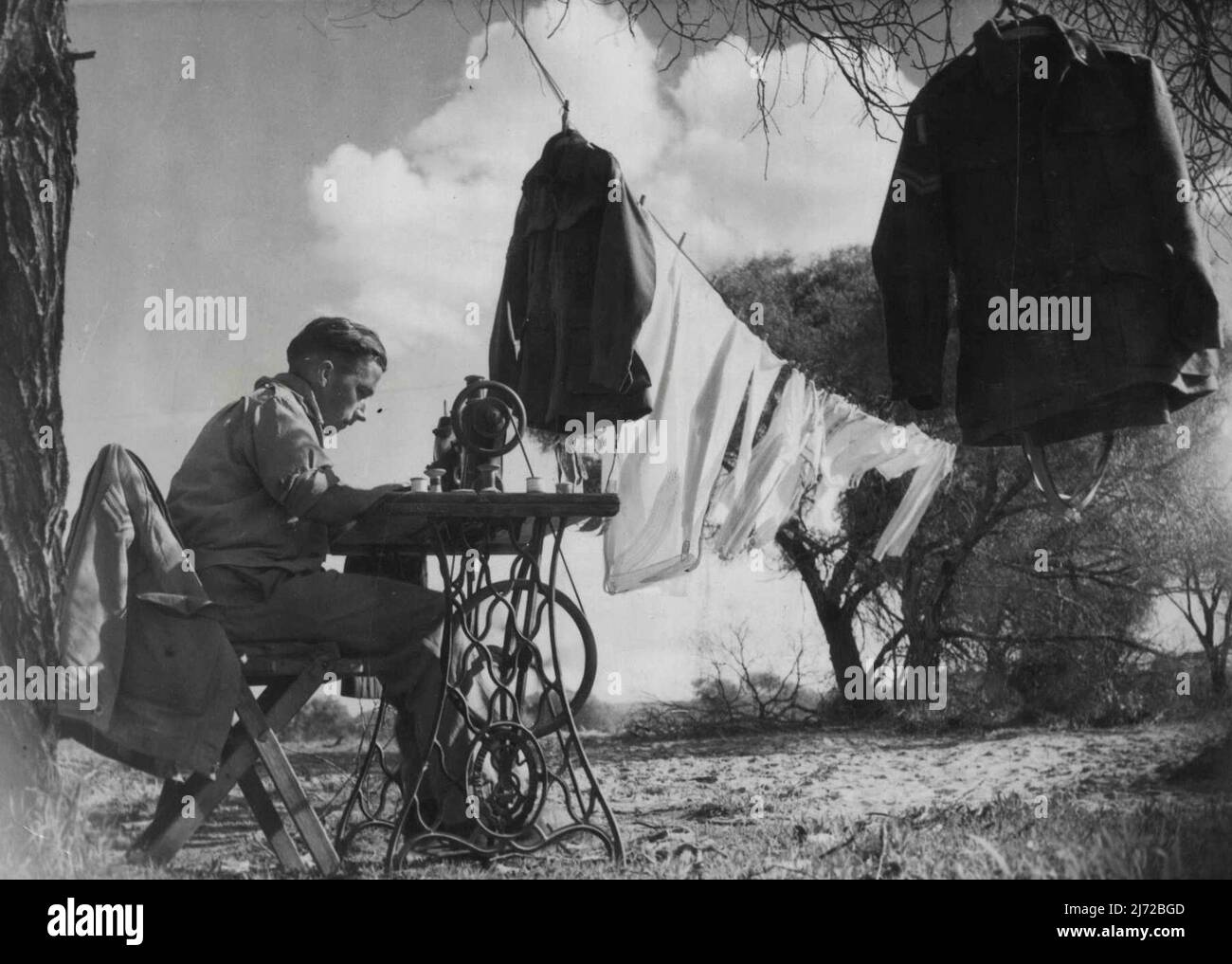 Cpl. N.E. Sully benutzte eine Nähmaschine, um seine Armeeuniformen zu reparieren. Ein Teil der Kleidung, die hinten in der Schlange steht, durchläuft auch seine Maschine. 3. September 1943. (Foto von H. Rodda). Stockfoto