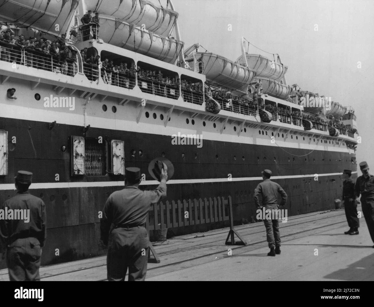 Es gibt einen Digger an Bord ohne seine Kopfbedeckung. Ein US-Soldat winkt mit einem lachigen Hut fröhlich zum Abschied, als sich die SS New Australia auf den Auszug aus dem Wharf in Pusan vorbereitet. Nach zwölf Monaten in Korea bringt das Schiff 2. Milliarden der Royal Australian Regt nach Australien. 15. April 1954. (Foto von Brit Com PR Photo). Stockfoto