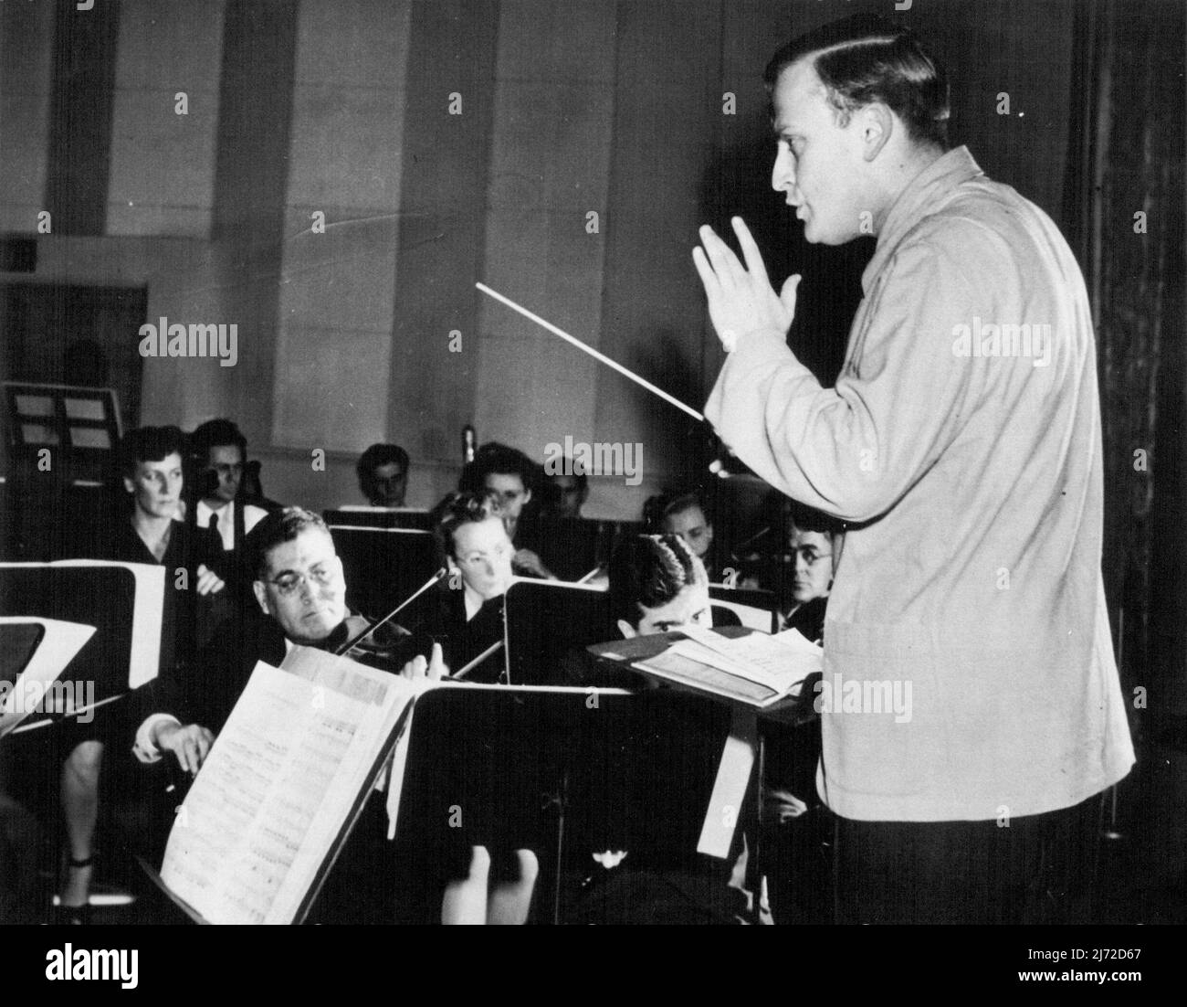 Menuhins Debüt als Dirigent -- Yehudi Menuhin gibt hier sein Debüt als Orchesterdirigent und leitet das Dallas Symphony Orchestra in einer Radiosendung. Die Geigerin folgte damit anderen Konzertkünstlern, die ihre Ambitionen erfüllt haben, den Baton zu winken, bevor sie das Podium bestritt. Menuhin hatte bei seinem Freund Antal Dorati, dem ständigen Dirigenten des Dallas Orchestra, Dirigiertechnik studiert. Dorati, die geplant hatte, das Radio-Konzert zu besuchen, wurde auf einer Flugreise aus New York in St. Louis gegründet. 22. Januar 1947. (Foto von Wide World Photo). Stockfoto