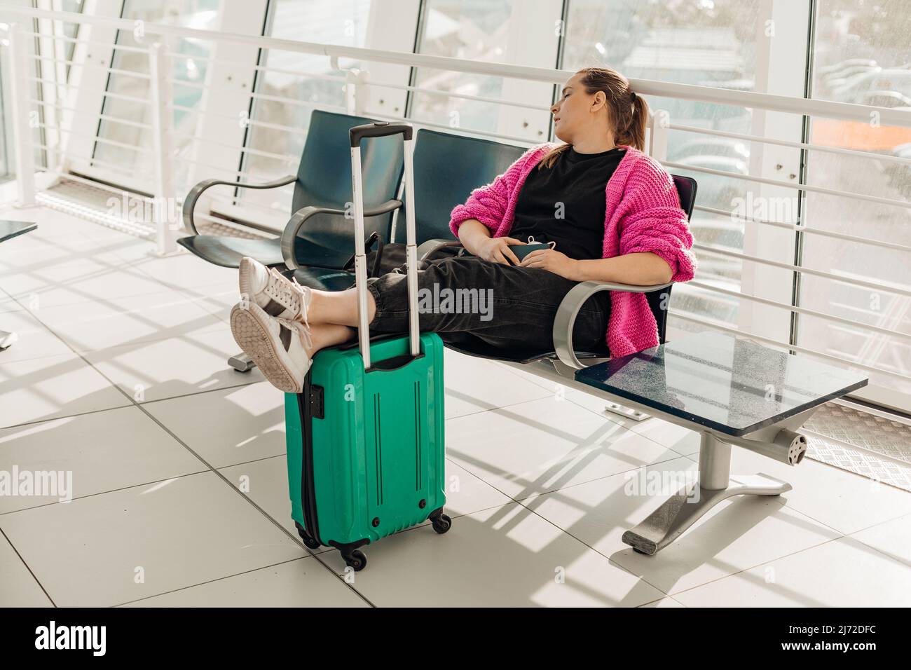 Geschäftsfrau mit Gepäck, Beine auf Koffer halten, rosa Jacke tragen, nach dem Flug im vip-Wartezimmer am Flughafen schlafen Stockfoto
