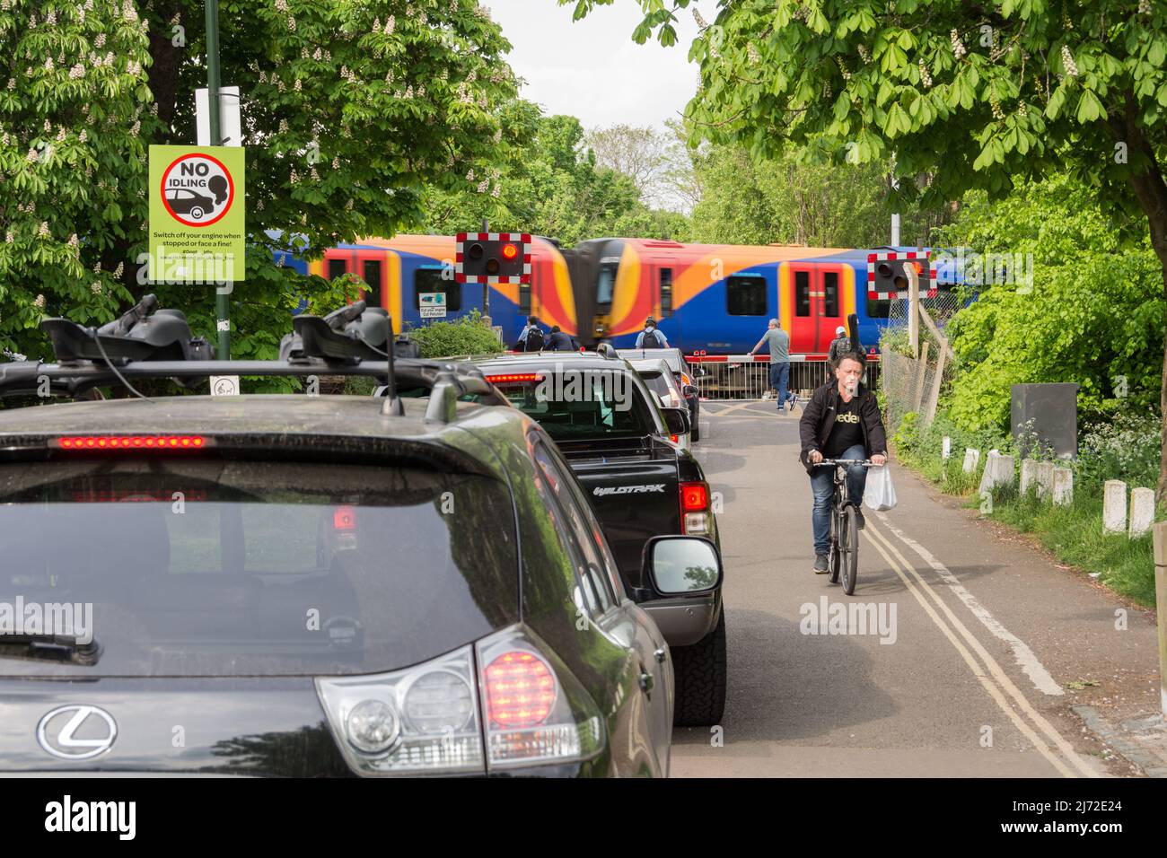 Stationäre Autos stehen Schlange und stehen im Leerlauf, während ein Zug der South Western Railway die Signalbox Vine Road von Network Rail in Barnes, London, SW13, England, Großbritannien, passiert Stockfoto