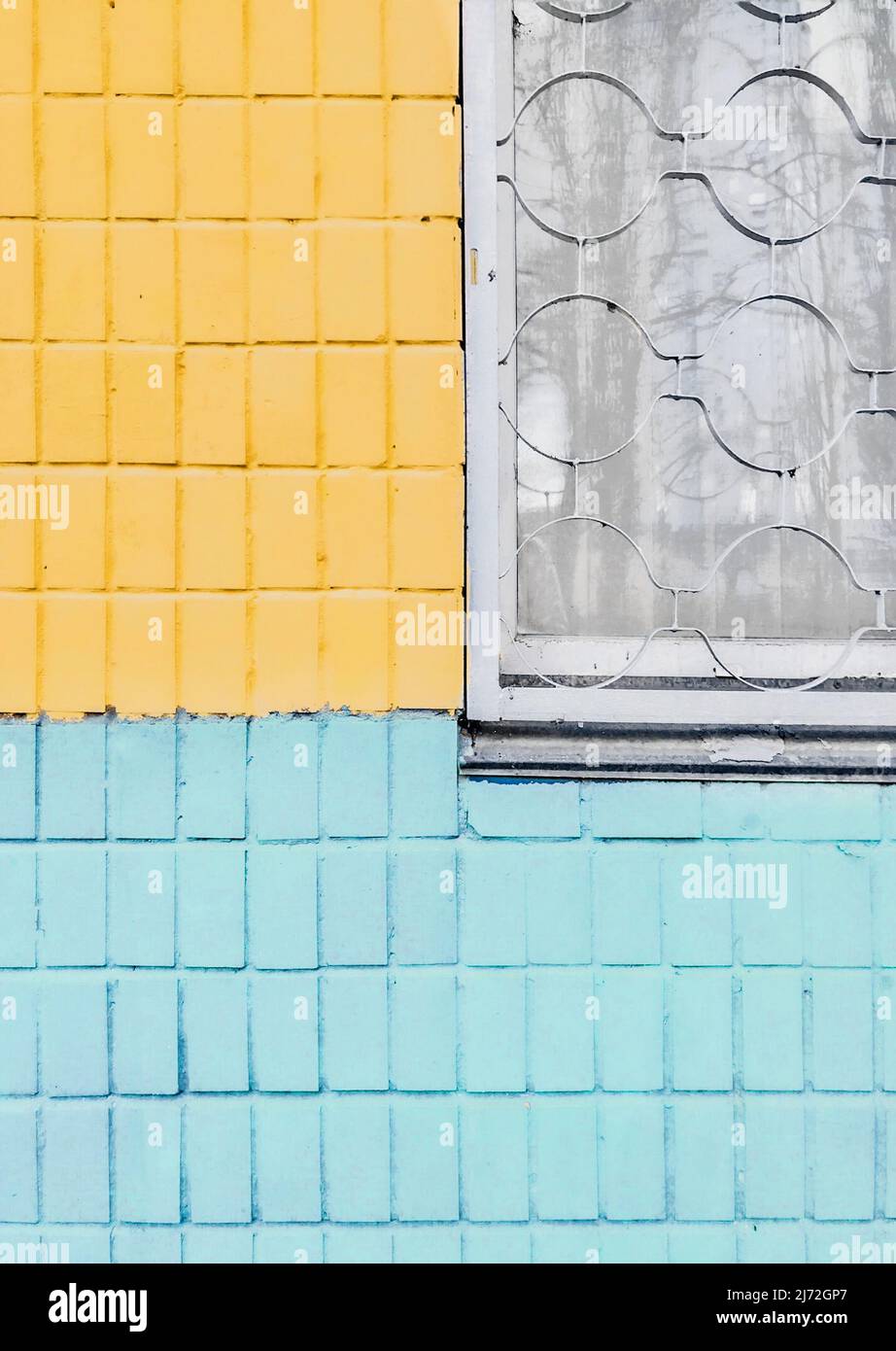 Blau und gelb gestrichene Fliesenwand mit Fenster und Metallgitter darauf. Stockfoto