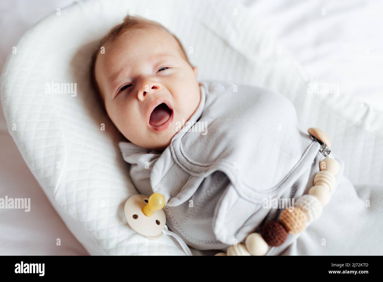 Niedliches blondes kaukasisches Baby zwei Monate alt, das zu Hause im Kokon liegt und gähnt Stockfoto