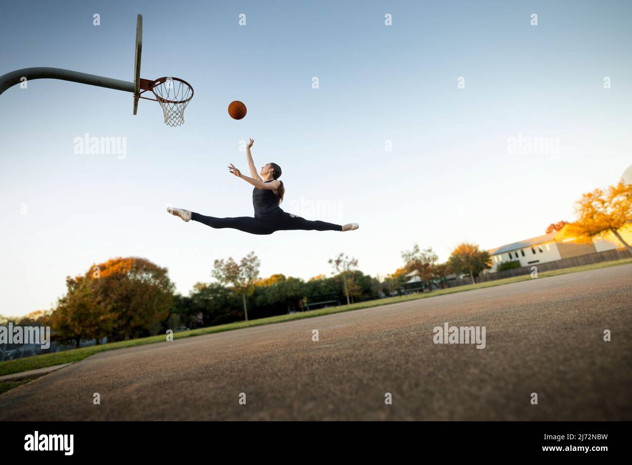Balletttänzerin im Mittelluftspringen, die auf einem Platz im Freien Basketball spielt Stockfoto
