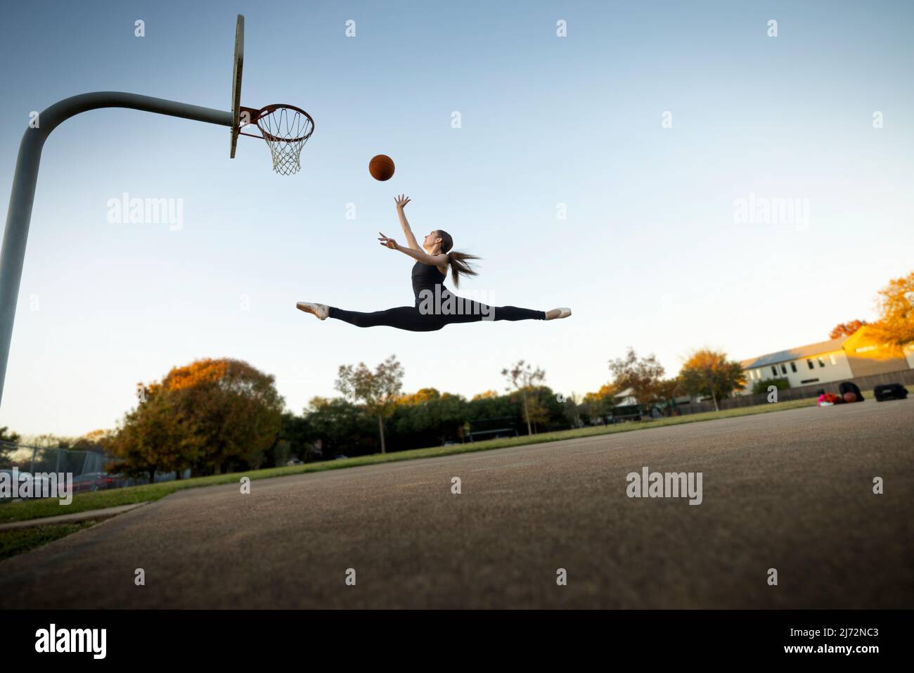 Balletttänzerin, die auf einem Platz im Freien Basketball spielt Stockfoto
