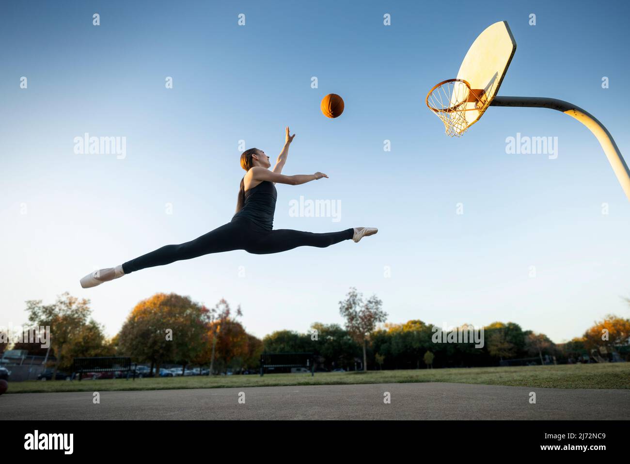 Balletttänzerin springt und schießt Körbe auf einem Basketballplatz im Freien Stockfoto