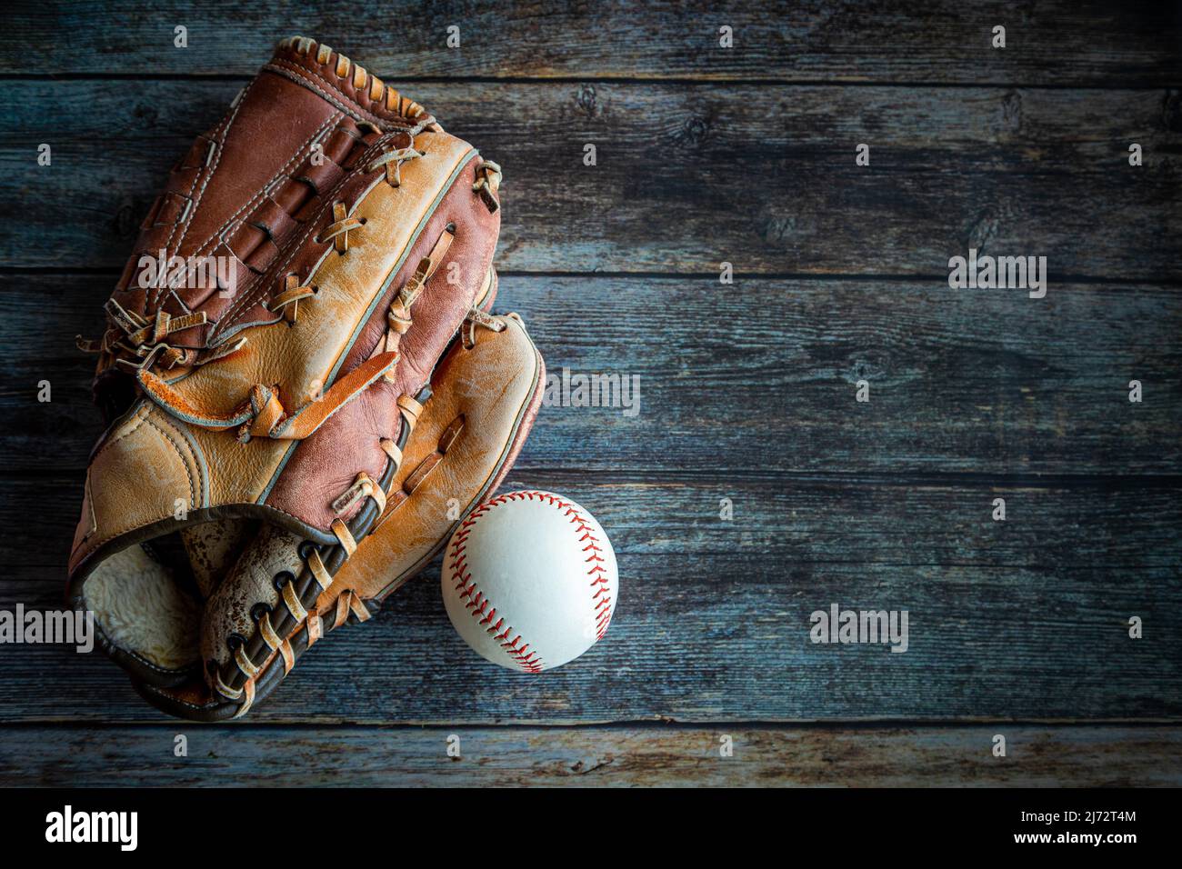 Leder-Baseballhandschuh oder Softballhandschuh mit Ball auf rustikalem Holzhintergrund mit Kopierfläche. Stockfoto