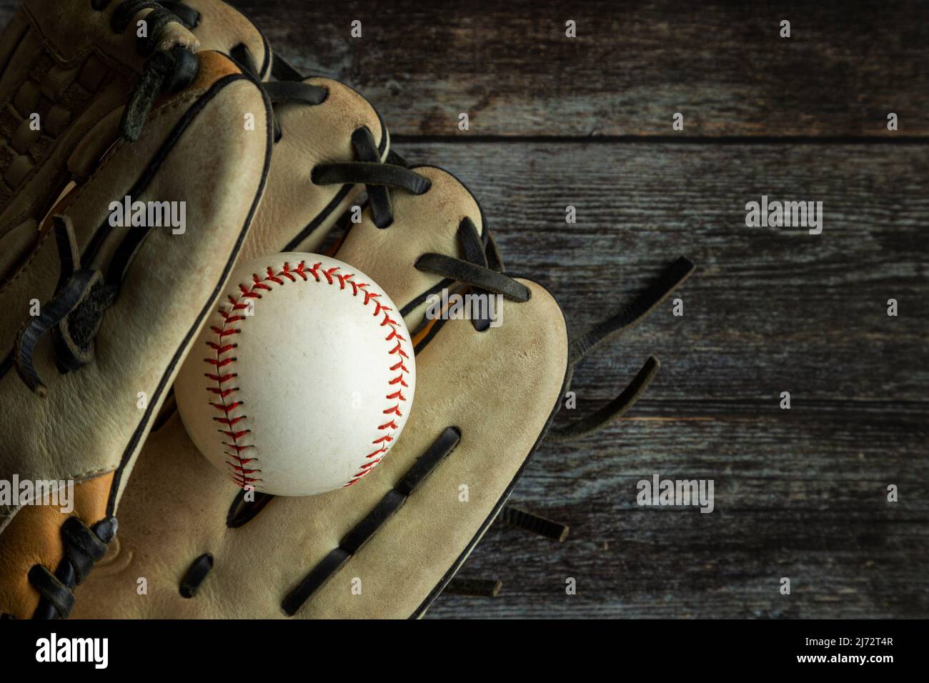 Leder-Baseballhandschuh oder Softballhandschuh mit Ball auf rustikalem Holzhintergrund mit Kopierfläche. Stockfoto