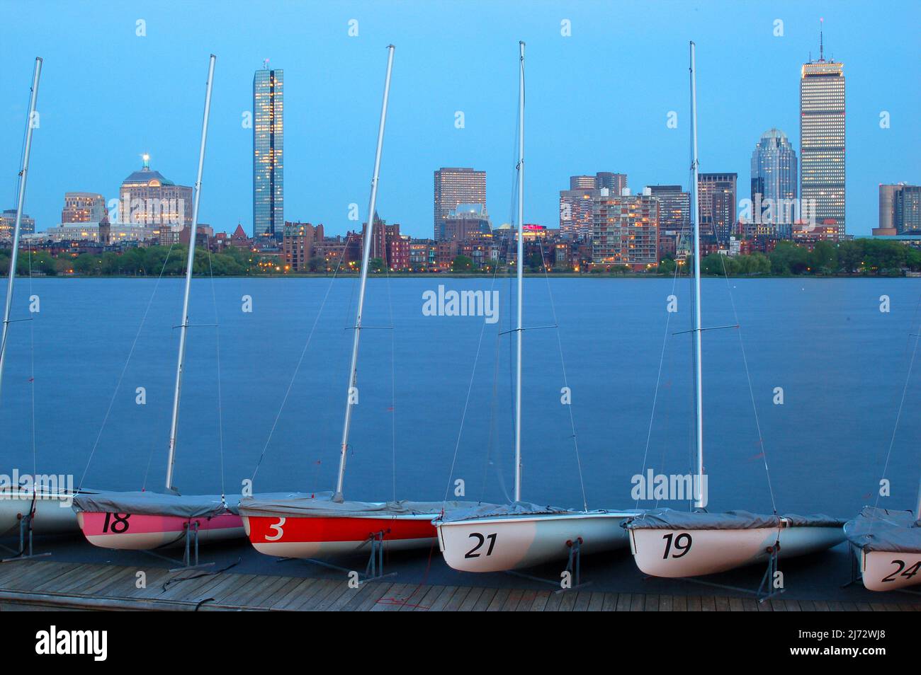 Kleine Segelboote stehen an den Docks am Charles River an, während die Lichter der Skyline von Boston beginnen zu leuchten Stockfoto