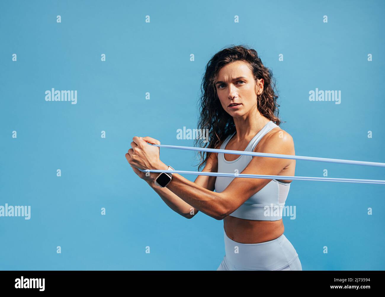 Porträt des jungen Fitness-weiblichen Trainings mit Widerstandsband auf blauem Hintergrund Stockfoto