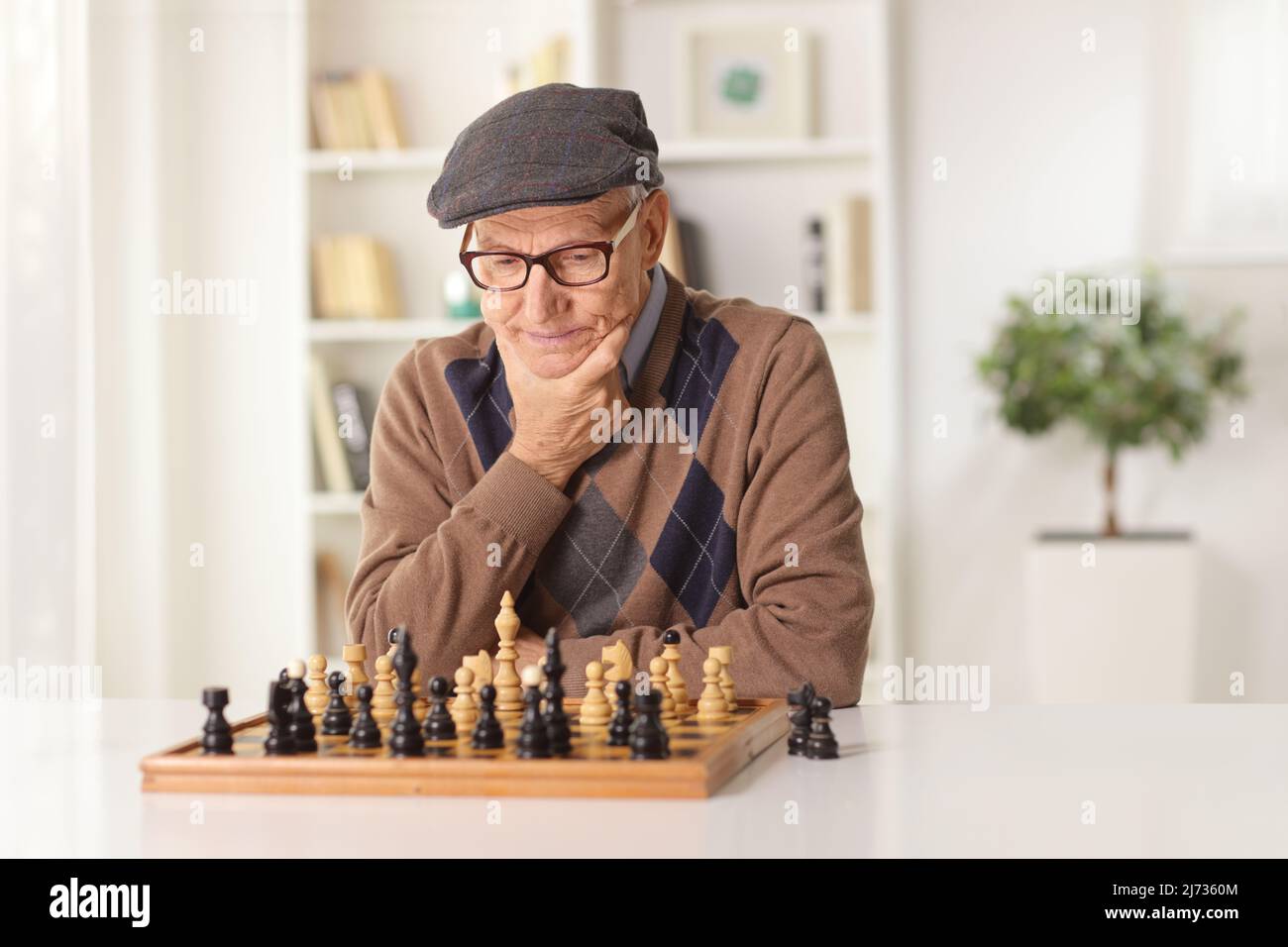 Älterer Mann, der alleine an einem Tisch zu Hause Schach spielt Stockfoto