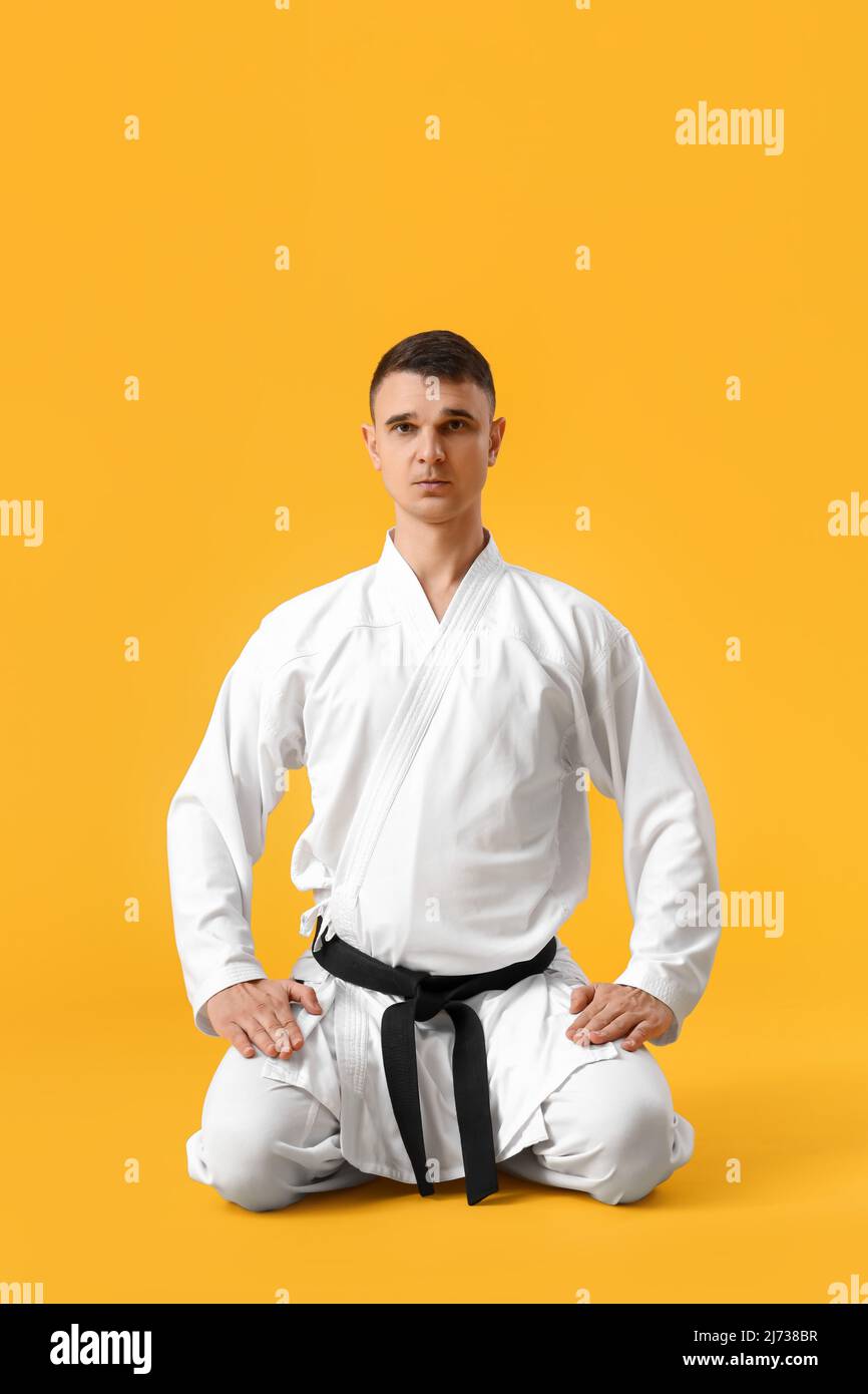 Männlicher Karate-Ausbilder sitzt in Seiza auf gelbem Hintergrund Stockfoto