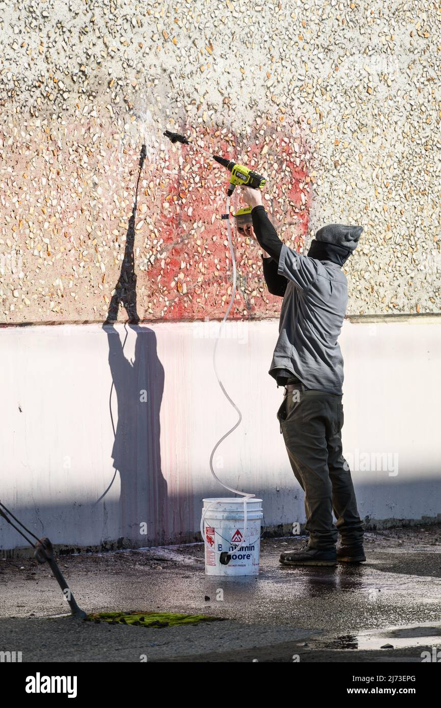 Seattle - 06. Februar 2022; Arbeiter, der mit einer Spritzpistole übermalte Graffiti von einer Wand in Seattle entfernt Stockfoto