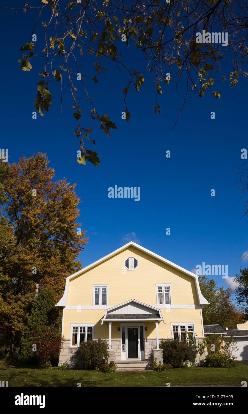 Gelbes zweistöckiges Haus mit Stein- und Holzplanken im Scheunenstil mit landschaftlich gestaltetem Vorgarten im Herbst. Stockfoto