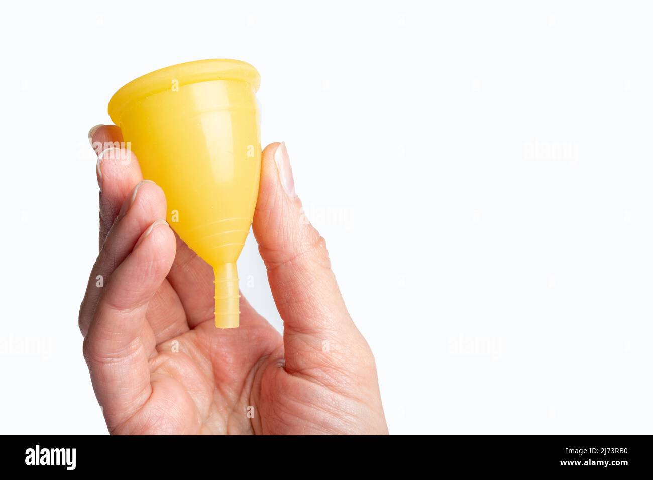 Hand mit einer gelben Menstruationsschale auf weißem Hintergrund. Frauengesundheitskonzept. Umweltfreundliches Konzept. Zero Waste Konzept. Stockfoto