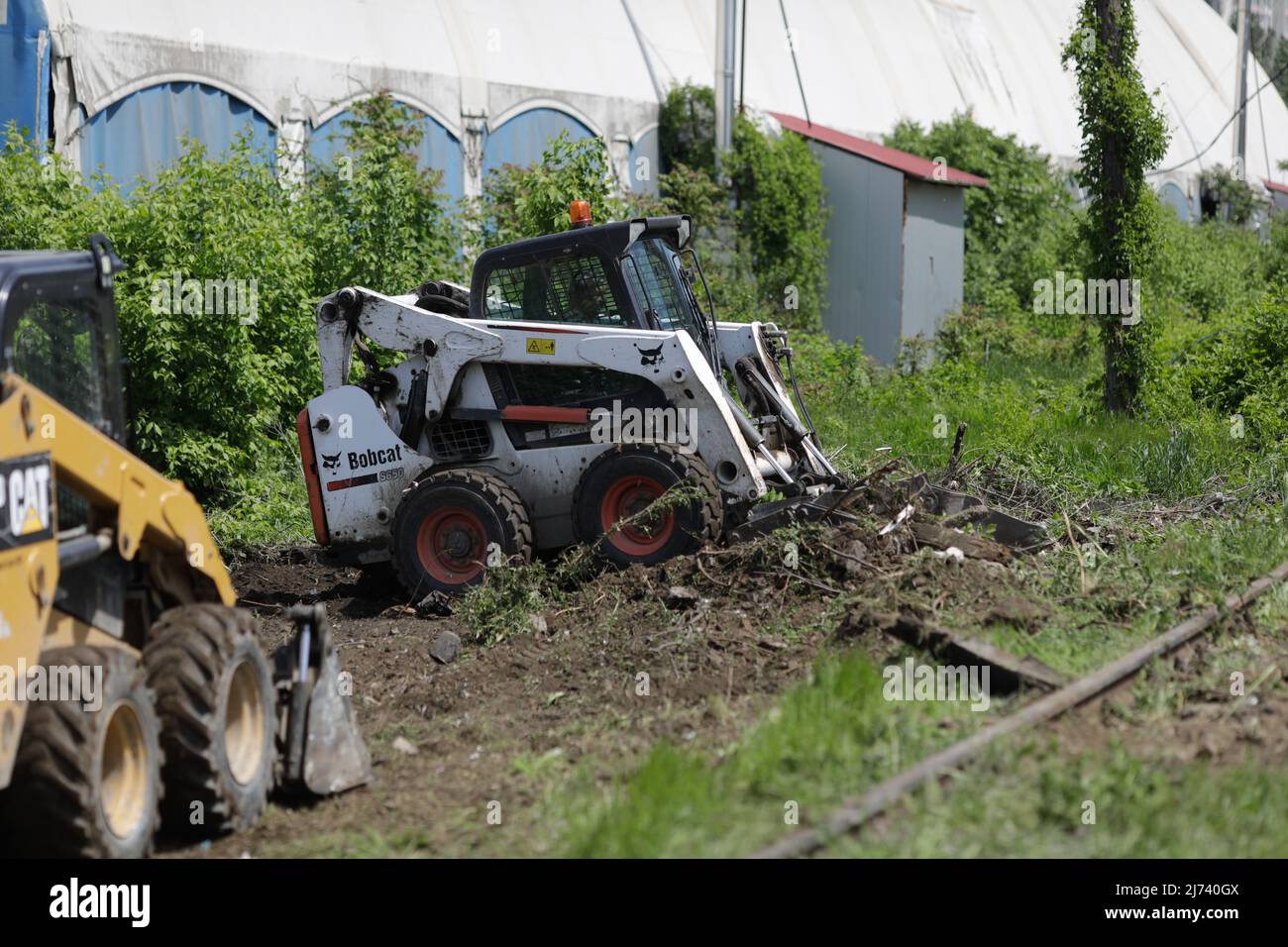 Bukarest, Rumänien - 1. Mai 2022: Arbeiter säubern ein Gebiet von Vegetation und Eisenbahnschutt für zukünftige Bauarbeiten. Stockfoto