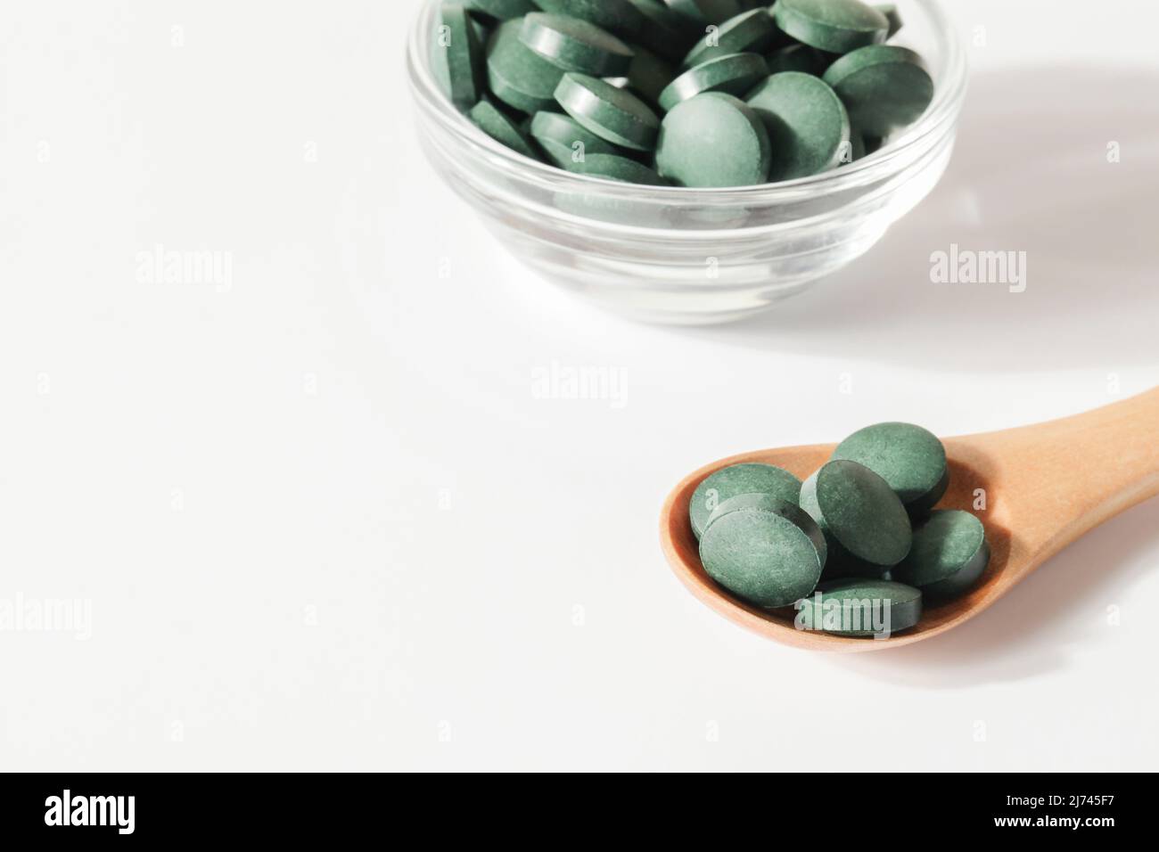 Natürliche Zusatzstoffe und Superfood. Grüne Spirulina Algenpillen in Löffel und Glasschale auf weißem Hintergrund. Gesunde concept.organic Lebensmittel kopieren Raum Stockfoto