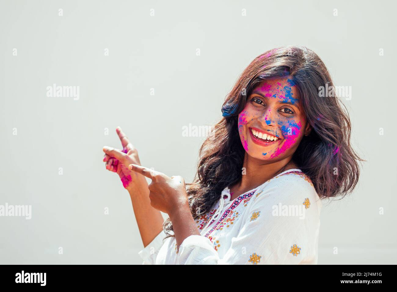 Holi Festival Der Farben. Porträt von glücklichen indischen Mädchen in holi-Farbe. Sie zeigt die Finger auf Copyspase weißen Studio-Hintergrund Stockfoto