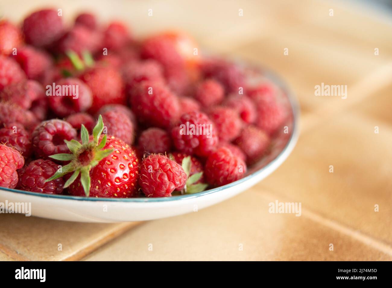 Teller mit frischen Erdbeeren und Himbeeren in einer Küche, auf beigefarbenen Bodenfliesen gelegt Stockfoto