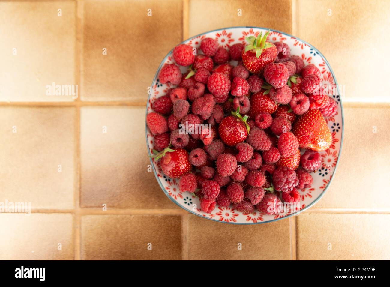Oben und große Ansicht eines Tellers mit frischen Erdbeeren und Himbeeren in einer Küche, die auf einem beigefarbenen Bodenfliesen ausgelegt ist Stockfoto