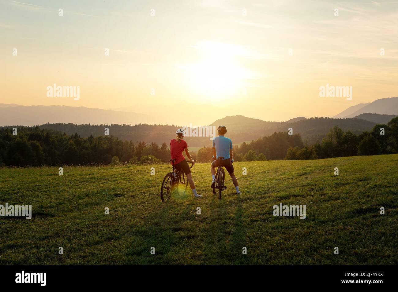 Frau und Mann, Rennfahrer, sitzen auf Fahrrädern, genießen eine schöne Berglandschaft bei Sonnenuntergang Stockfoto