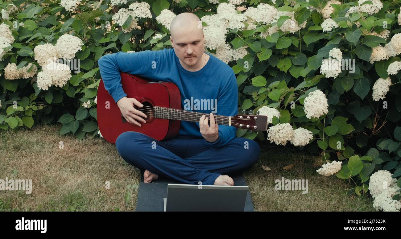 Mann mit Gitarre in Park Natur streamt online Podcast mit Gadgets Stockfoto