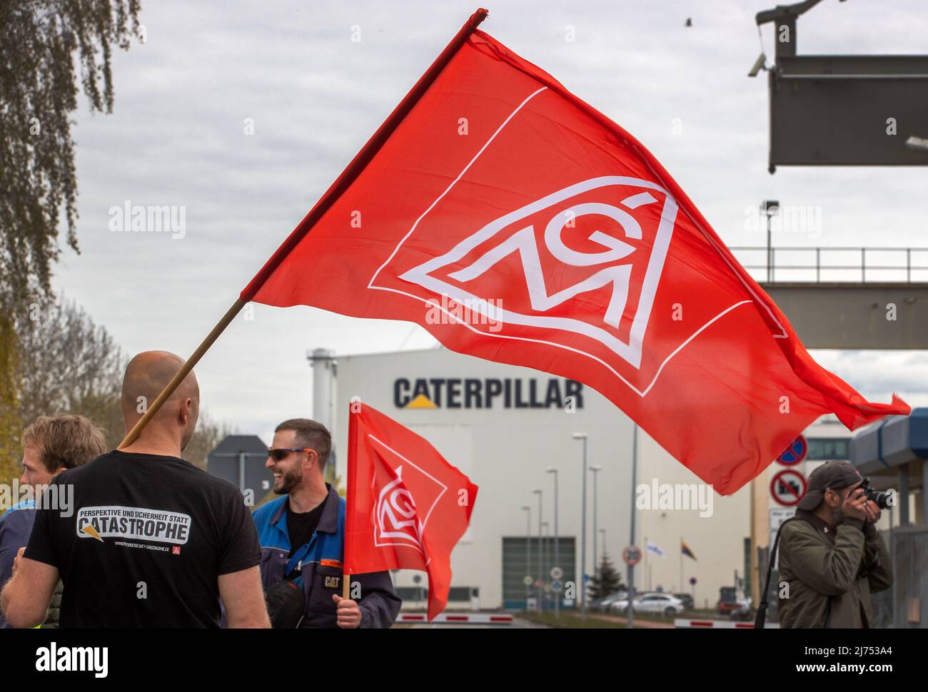 06. Mai 2022, Mecklenburg-Vorpommern, Rostock: Mitarbeiter von Caterpillar-Motoren stehen während eines Warnstreiks vor dem Werkstor. Bisher haben die Verhandlungen über den Sozialtarifvertrag zu keinen nennenswerten Fortschritten geführt. Mit der geplanten Schließung des Standorts am 31. Dezember 2022 sind 120 Mitarbeiter mit Arbeitsplatzverlusten konfrontiert. Foto: Jens Büttner/dpa Stockfoto