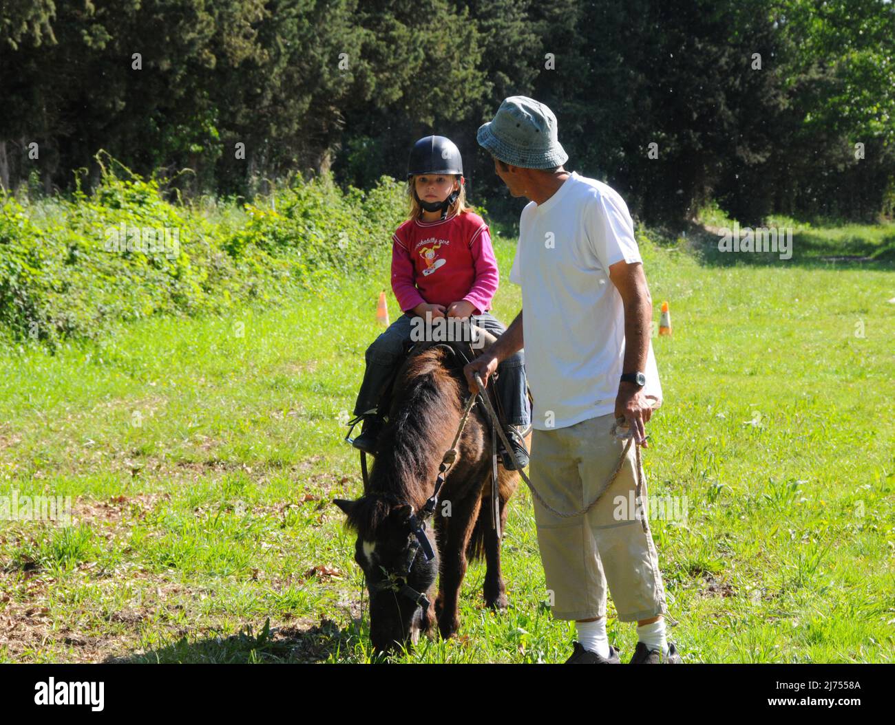 Junges Mädchen Reiten poney mit Vater hilft am sonnigen Tag Hobby oder Aktivität während der Ferien. Stockfoto