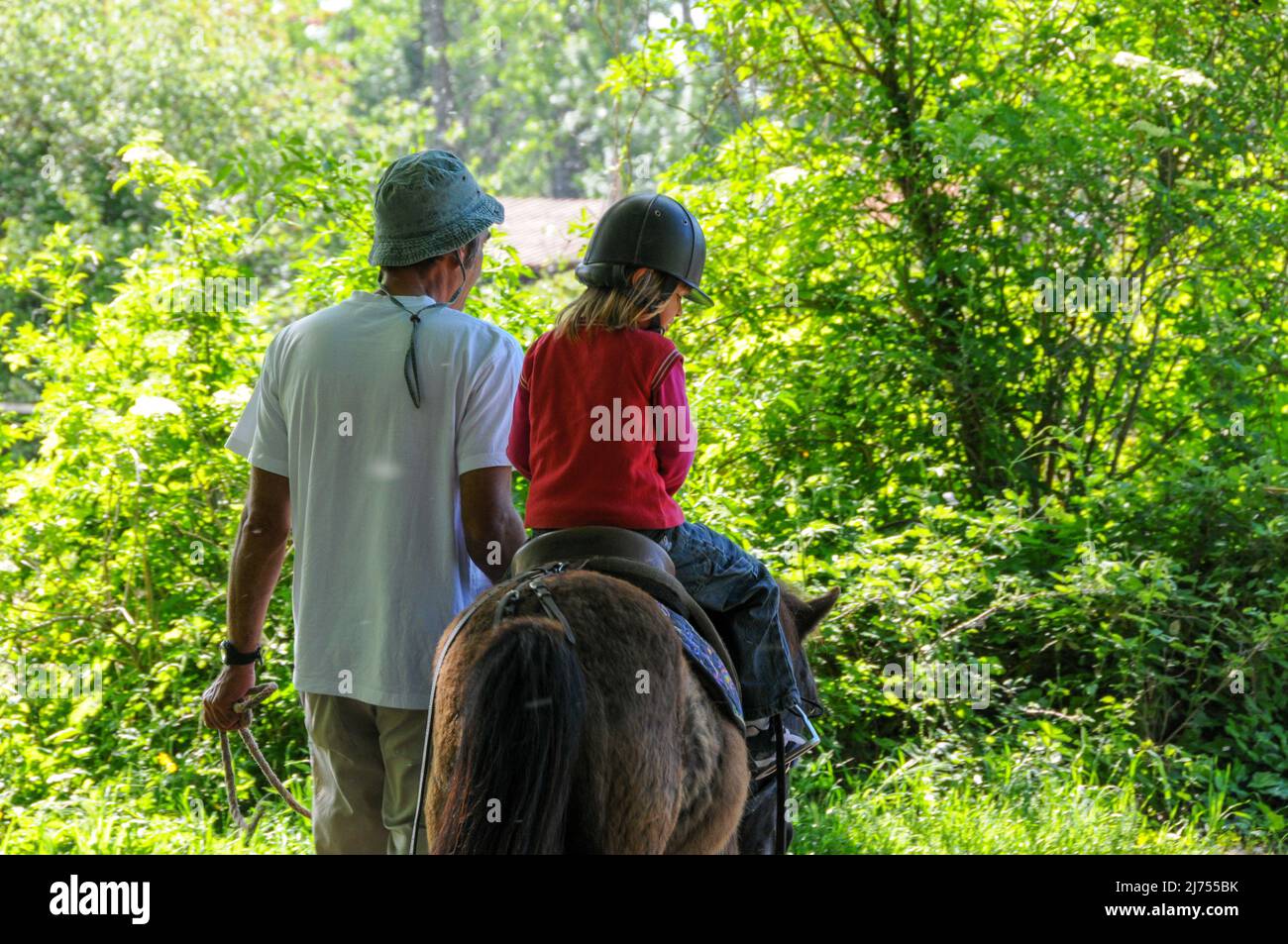 Junges Mädchen Reiten poney mit Vater hilft am sonnigen Tag Hobby oder Aktivität während der Ferien. Stockfoto