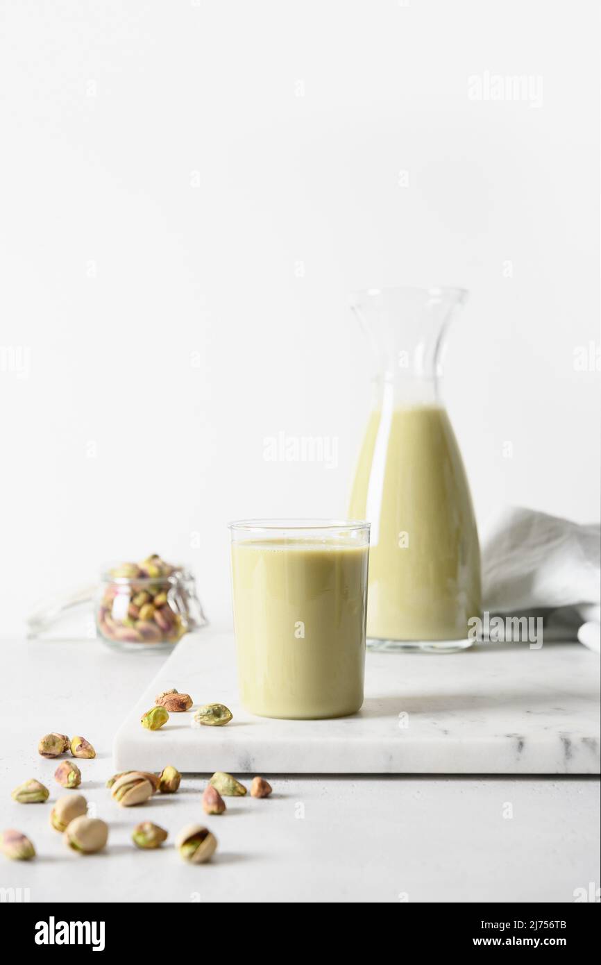 Pistazien-Milch im Krug und Pistazien auf weißem Hintergrund. Vegane nussige Milch auf pflanzlicher Basis und laktosefreie Milch. Vertikal. Stockfoto