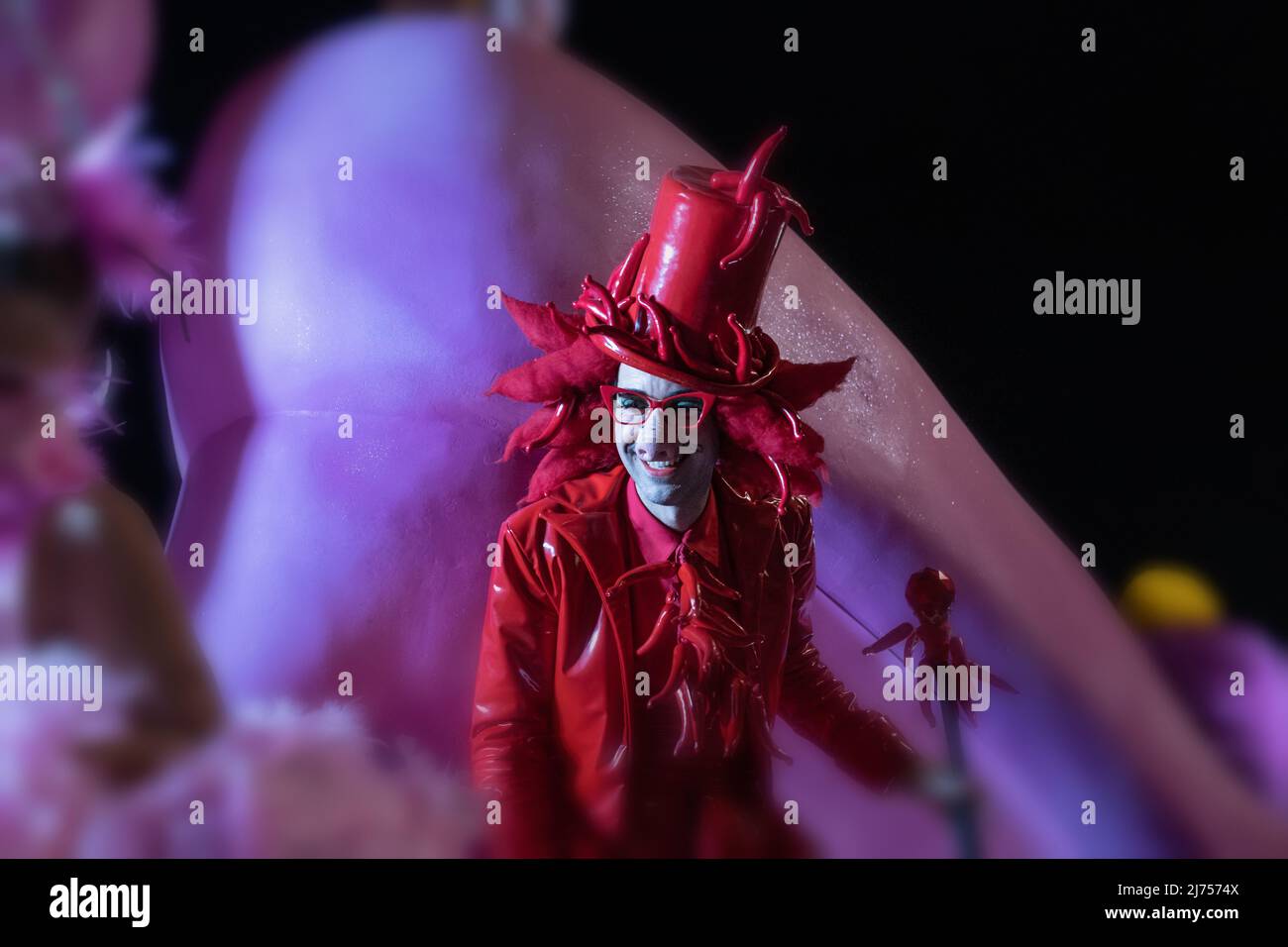 Karneval in Sitges, Spanien: Ein Nachtschwärmer, der eine bizarre Verkleidung mit einem Zylinderhut und Dutzenden von Paprika trägt, die alle streng rot sind, gibt ein Lächeln ab. Stockfoto