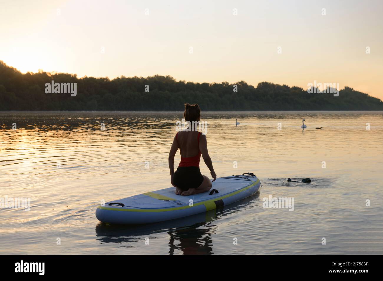 Eine Frau bereitet ihr Paddle Board für ihr morgendliches Yoga-Training auf einem ruhigen See vor Stockfoto