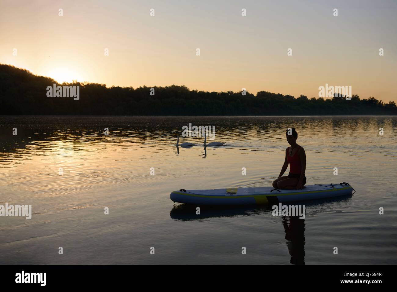 Sommermorgen Sonnenaufgang mit einer Frau, die Yoga auf ruhigem Wasser macht Stockfoto