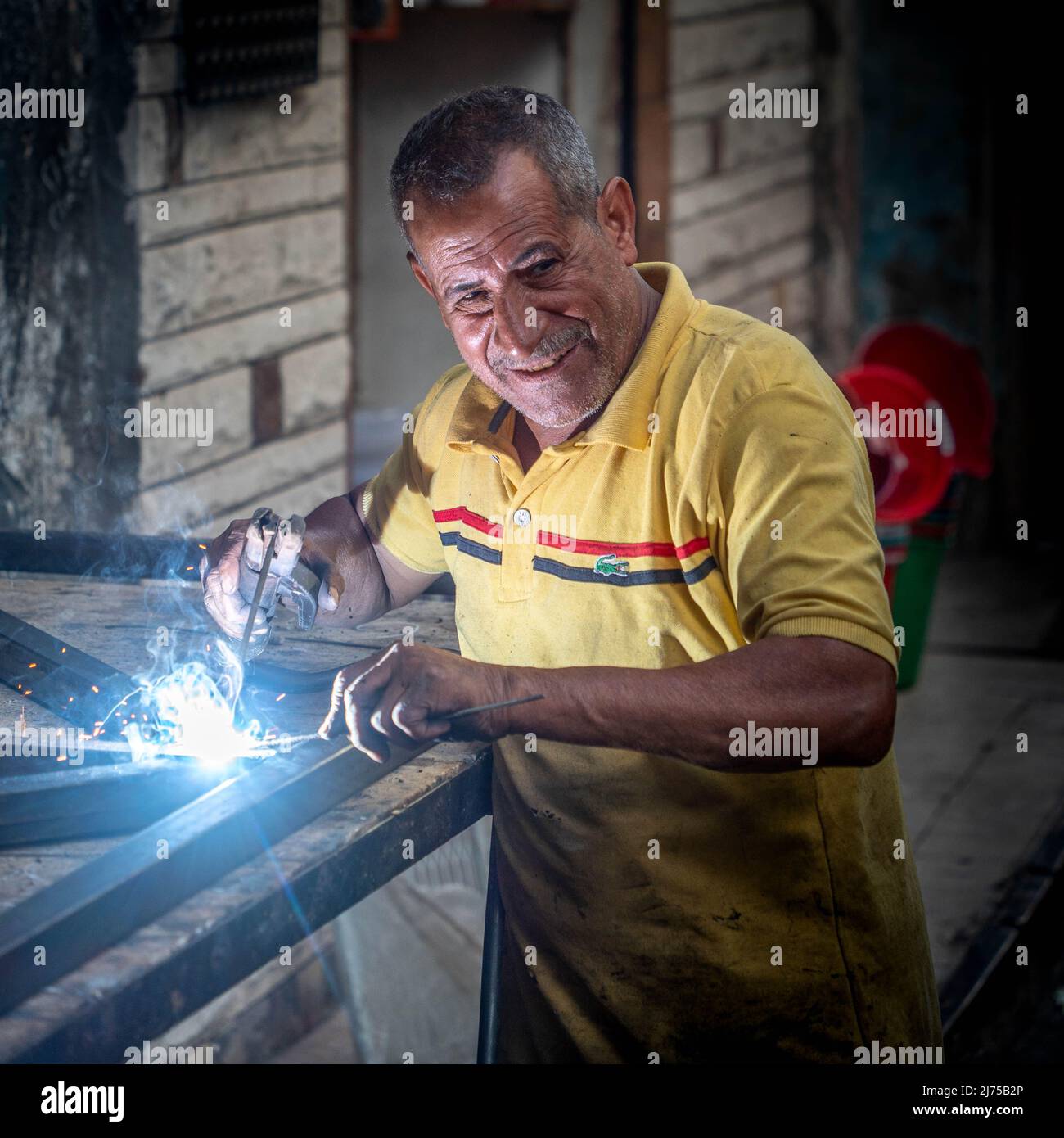 Alexandria, Ägypten - 21. Dezember 2021: Ein Mann arbeitet mit einem Schweißer in einer kleinen Straßenwerkstatt ohne Maske, lächelnd Stockfoto