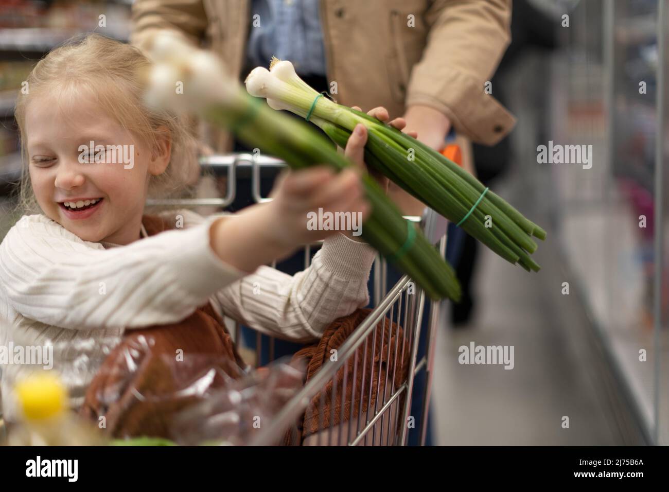 Kleines Mädchen, das während des Familieneinkaufs im Supermarkt auf dem Trolley sitzt Stockfoto