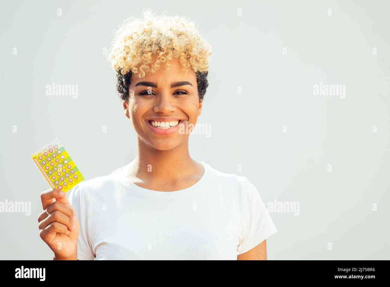 brasilianisches Mädchen mit niedlichen afro blonde Locken zeigt Kontrazeptiva Pillen in Studio weißen Hintergrund Stockfoto