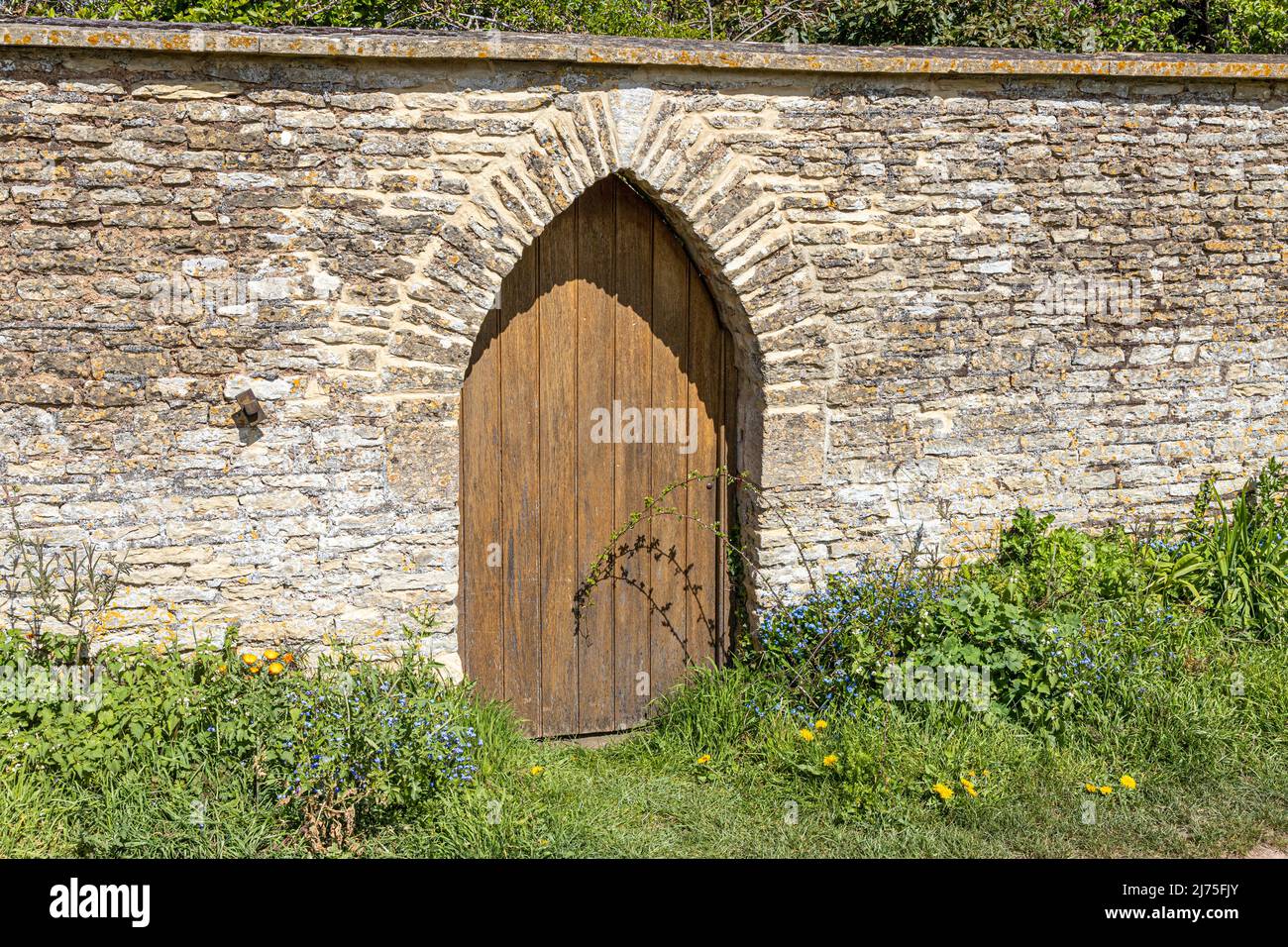 Ein einladender Bogeneingang in einer Steinmauer im Garten in Gloucestershire, England Stockfoto