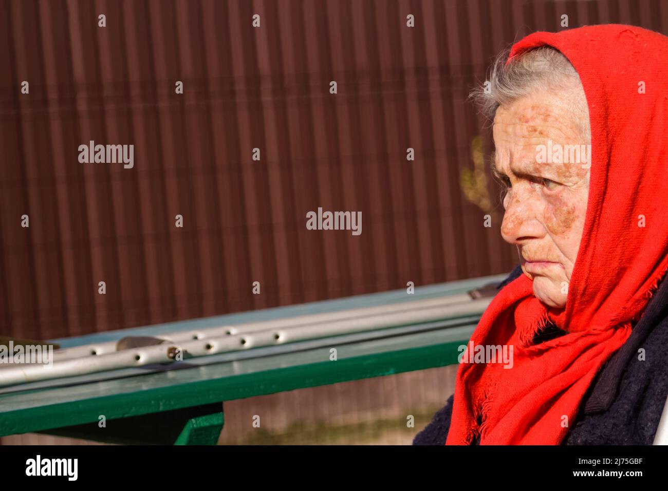 Defokussieren sie die ältere ukrainische Frau in einem roten Schal mit Krücken, die draußen sitzen. Frau 85 Jahre alt. Einzelperson. Nahaufnahme. Krank und heimatverbunden. Traurig Stockfoto