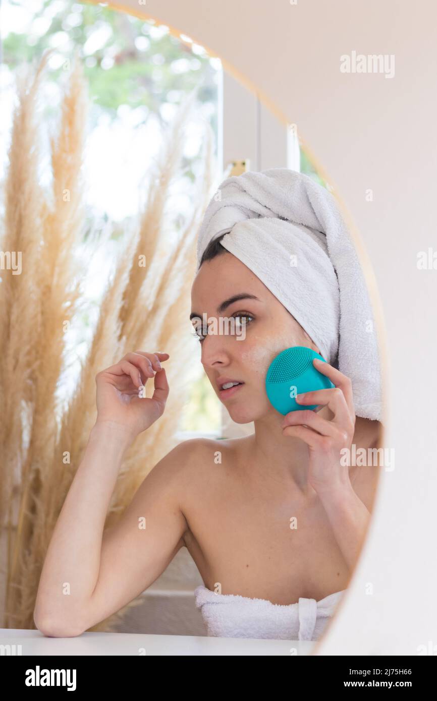 Junge Frau, die bei morgendlichen Hygieneverfahren im Bad die Gesichtshaut mit einem speziellen Ultraschallgerät säubert. Hautpflege- und Wellness-Konzept Stockfoto